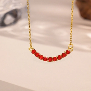 Minimalist gold necklace with red rhinestone smile pendant on warm white background