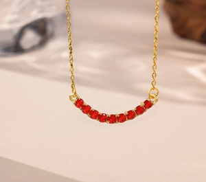 Close-up of golden necklace with 11 red round gemstones in a curved smile design