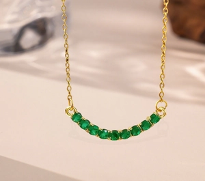 Macro shot of gold necklace featuring a smile pendant set with 11 green round gemstones