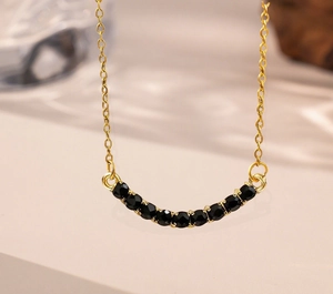 Detail shot of a curved gold smile necklace inlaid with shimmering black gemstones