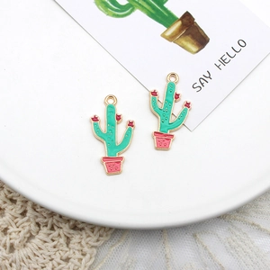 Macro detail of green cactus enamel charms for DIY jewelry making on a white ceramic plate