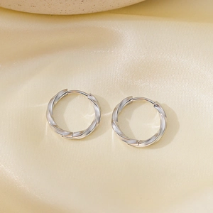 Detailed view of silver Mobius twist hoop earrings on smooth yellow silk fabric