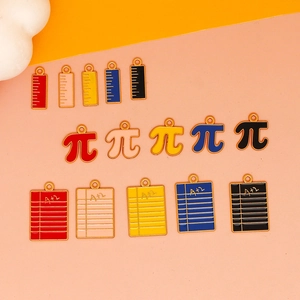 Nahaufnahme bunter Emaille-Anhänger in Form von Lineal, Pi-Symbol und Notizbuch