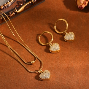 Detailopname van een elegante gouden dubbellaagse hartketting en bijpassende oorbellen.