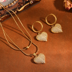 Detailopname van gouden ketting en oorringen met hartvormige bedeltjes in pavé