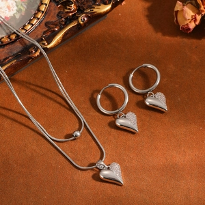 Close-up van elegante zilverkleurige hartjesketting en oorbellen sieradenset op warme achtergrond