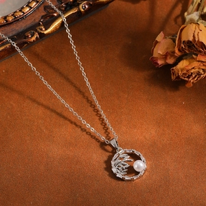 Primo piano di elegante collana color argento con ciondolo a perla e foglia di bambù