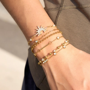 Macro view of layered 316 stainless steel gold bracelets with sparkling zircons on wrist.