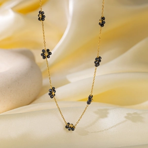 Collana a catenina dorata con piccoli ciondoli a fiori neri su morbido tessuto di seta