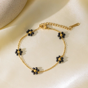 Collana con fiori dorati e perline nere sfaccettate su elegante tessuto di seta champagne