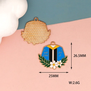 Close-up of enamel graduation gown charm with white flowers and "WE CAN DO IT" text detail