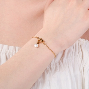 Dettaglio ravvicinato di un bracciale a nodo dorato con un elegante ciondolo di perla bianca.