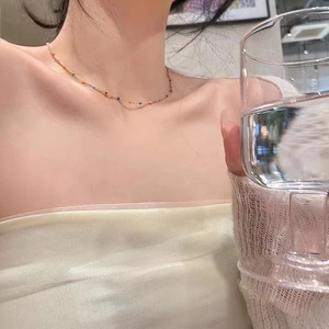 Minimalist multi-color beaded clavicle necklace in gold finish worn by model in home setting