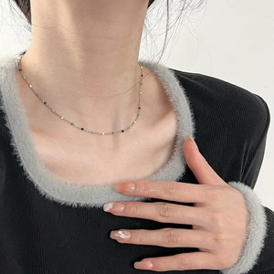 Minimalist gold titanium necklace with blue and white beads worn on a model's collarbone