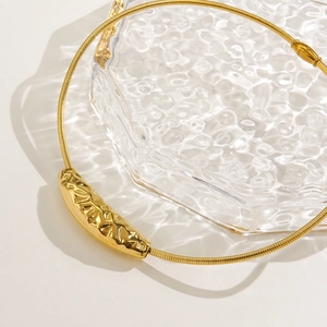 Close-up of a gold stainless steel torque necklace with a textured hammered bar pendant
