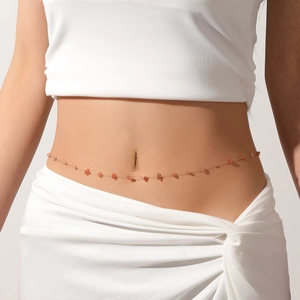 Close-up detail of a dainty gold-tone waist chain with irregular red stones on a model