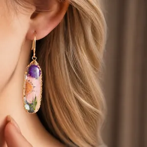 Elegant handmade resin oval earrings with dried flowers worn by a model in soft light
