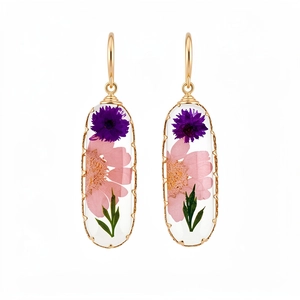 Elegant gold-framed oval resin earrings featuring real dried pink and purple flowers.