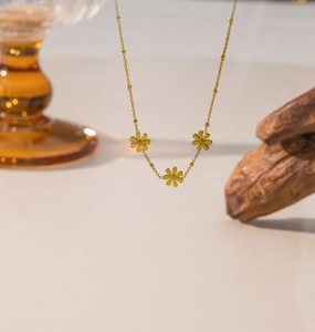 Dettaglio della collana dorata con tre ciondoli a margherita e catena a sfere opaca