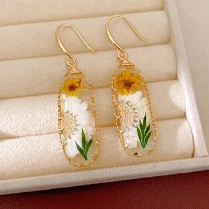 Detailed view of handmade resin oval earrings with yellow and white dried flowers