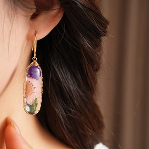 Close-up of sweet resin oval earring with pink and purple dried flowers on ear
