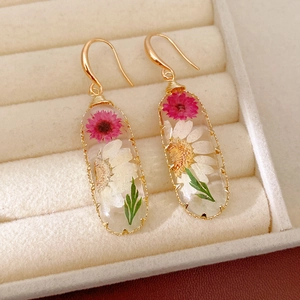 Close-up of resin oval earrings featuring real pink and white dried flowers.