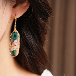 Close-up view of elegant resin oval earrings featuring real dried flowers and gold hooks