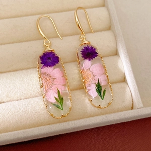 Detailed macro view of resin oval earrings featuring real dried flowers and gold hooks