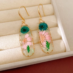 Detail view of sweet oval resin hook earrings with embedded real pink and teal dried flowers