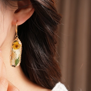 Close-up of elegant resin oval earrings featuring real dried yellow flowers and leaves