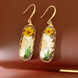Detailed view of handmade resin earrings with real dried flowers and gold-tone hooks.