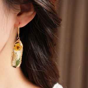 Close-up of handmade resin earring with real dried yellow and white flowers on a model.