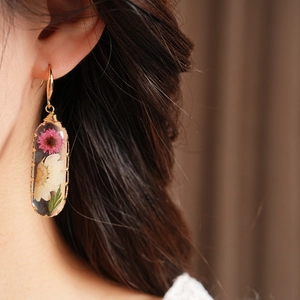 Close-up of handmade resin oval earrings with dried pink flowers worn by an Asian model.