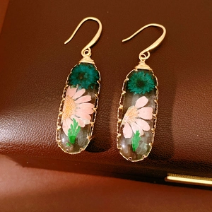 Close-up of sweet resin oval hook earrings with dried pink and teal flowers inside