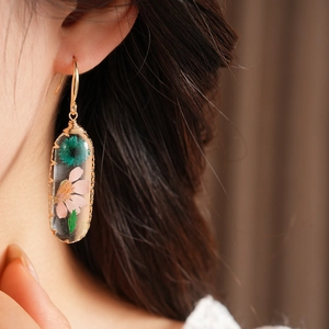 Detailed close-up of handmade resin oval earrings with preserved pink and green flowers