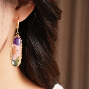 Close-up of resin oval earrings with embedded pink and purple dried flowers
