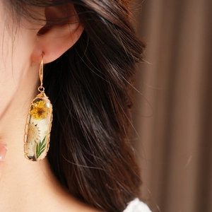 Close-up of elegant resin oval earrings featuring preserved yellow and white flowers
