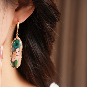 Macro detail of an elegant oval resin earring featuring real dried flowers worn on a model's ear