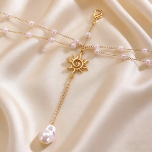 Macro detail of golden sunburst pendant and baroque pearl on silk satin background