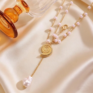 Close-up of layered gold body chain with snail pendant and pink baroque pearl