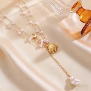 Close-up of gold shell pendant and pink pearl beads on a multi-layer body chain accessory.