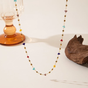 Detalle de collar de acero inoxidable dorado con cuentas de colores y cubos sobre fondo