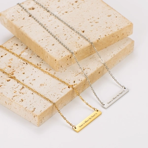 Vista macro del collar de barra grabado 'Home is Where the Heart is' en oro y plata