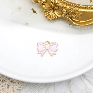 Primo piano di un ciondolo a fiocco in smalto rosa per gioielli fai-da-te con cornice dorata.