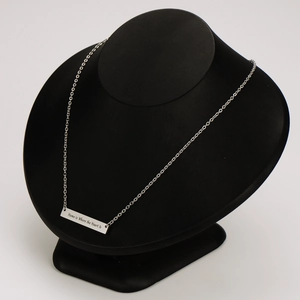 Primer plano del collar de barra grabado sobre un soporte de joyería negro