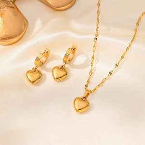 Détail d'un ensemble de bijoux cœur dorés avec collier et boucles sur fond de soie