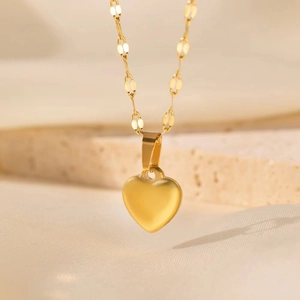 Vue macro du collier pendentif cœur en or brossé mat sur un support en pierre beige