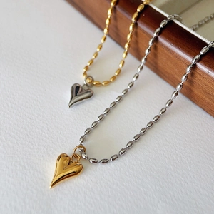 Two-tone heart pendants with gold and silver ball chains on minimalist white and wood background