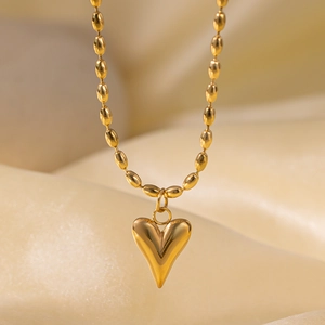 Close-up of a polished gold heart pendant on a bead chain necklace over silk fabric