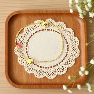Minimalist gold titanium steel heart bracelet with red string on white lace background